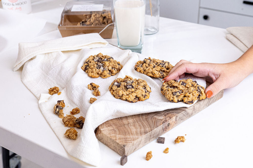 Cookies on a wooden board with a hand reaching for one, milk in the background